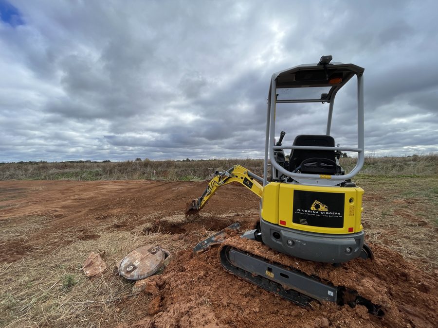 Rear view of the Riverina Diggers excavator showing the dry hire contact panel, working beside a tank lid